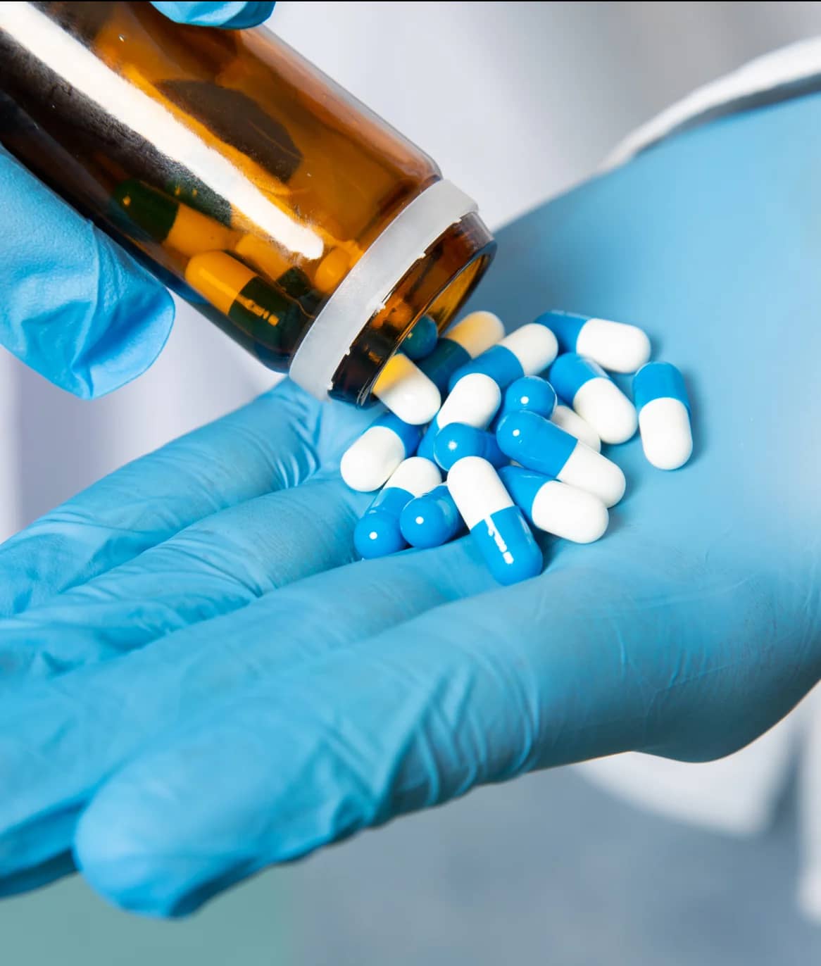 Gloved hand pouring capsules from a medicine bottle